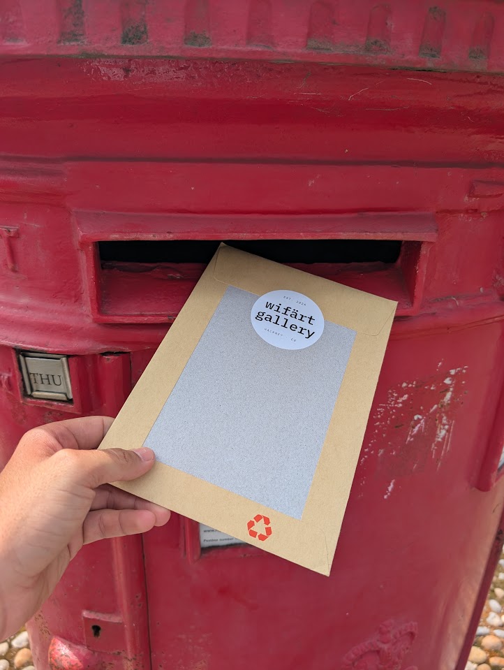 A kraft envelope with the wifärt gallery sticker being posted into a red pillar box.